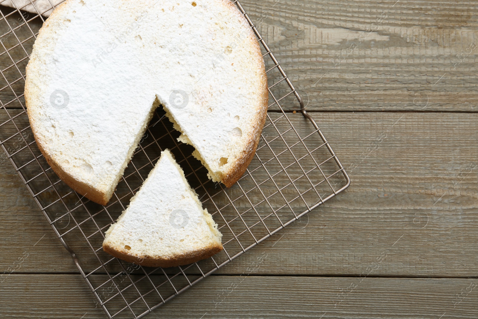 Photo of Delicious cut sponge cake with powdered sugar on wooden table, flat lay. Space for text