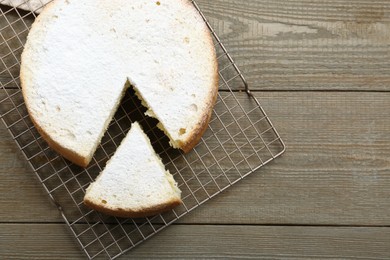 Delicious cut sponge cake with powdered sugar on wooden table, flat lay. Space for text