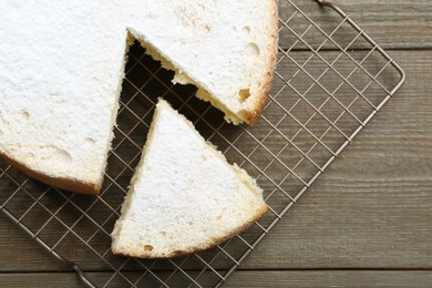 Photo of Delicious cut sponge cake with powdered sugar on wooden table, flat lay