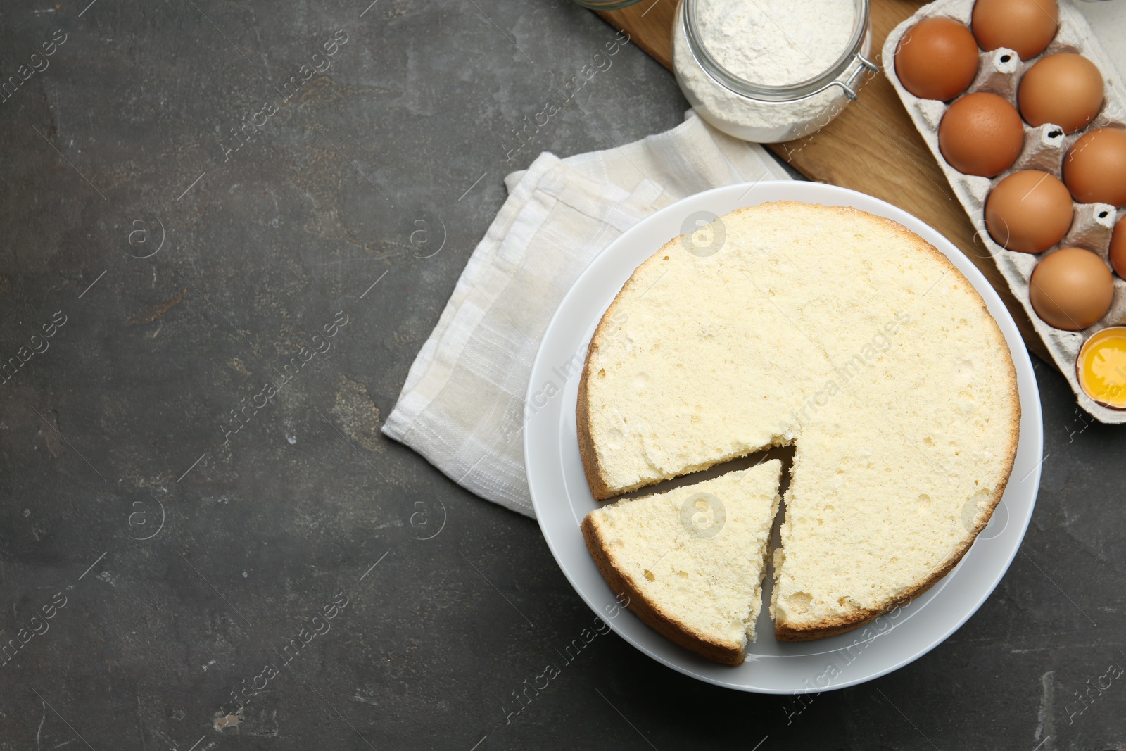 Photo of Delicious cut sponge cake and ingredients on grey textured table, flat lay. Space for text