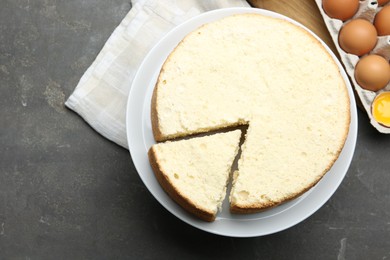 Photo of Delicious cut sponge cake and ingredients on grey textured table, flat lay