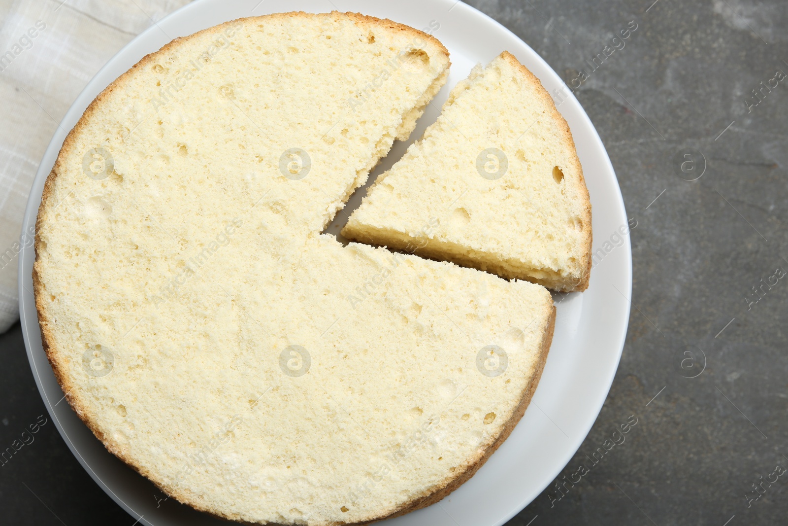 Photo of Delicious cut sponge cake on grey textured table, top view