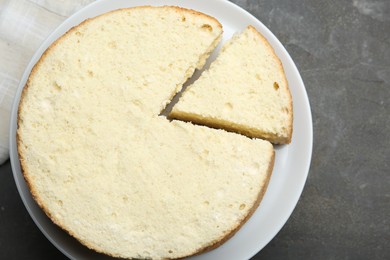 Photo of Delicious cut sponge cake on grey textured table, top view