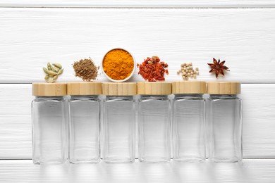 Photo of Different spices and glass jars on white wooden table, top view