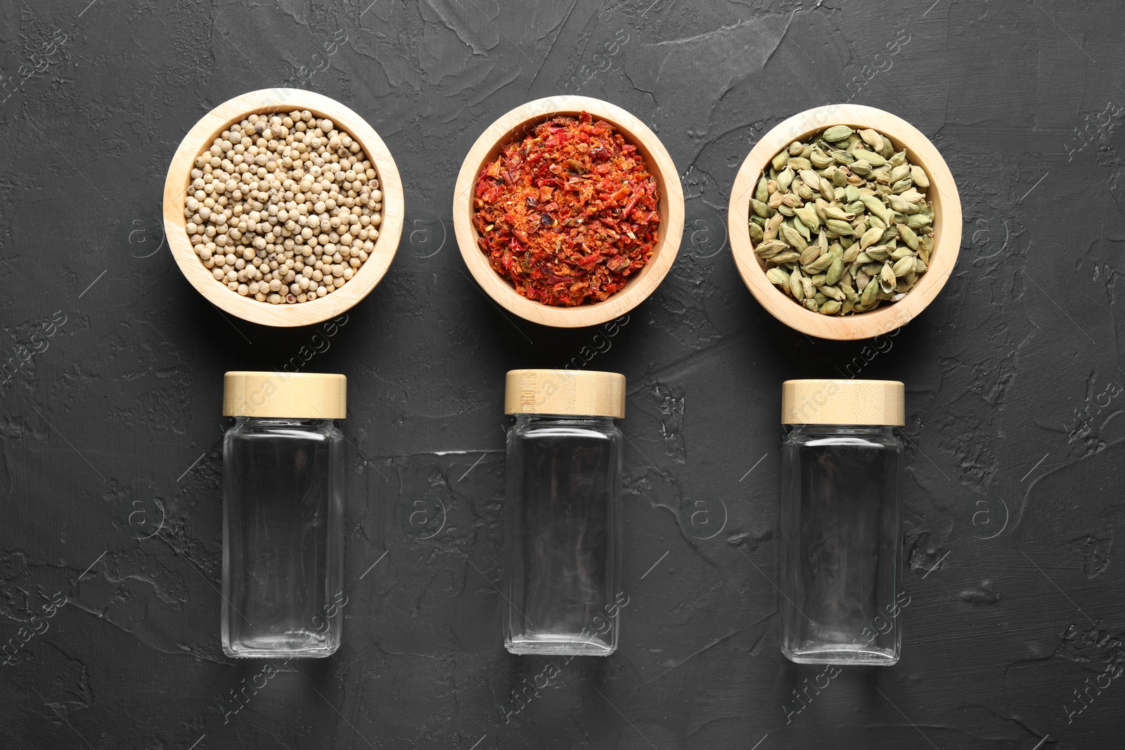 Photo of Different spices and glass jars on black table, flat lay