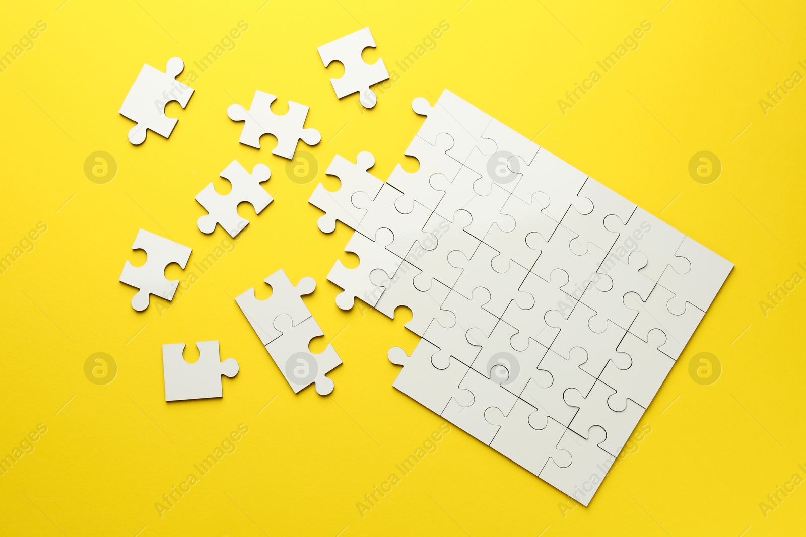 Photo of White puzzle pieces on yellow background, top view