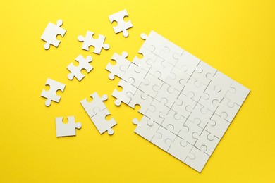 Photo of White puzzle pieces on yellow background, top view