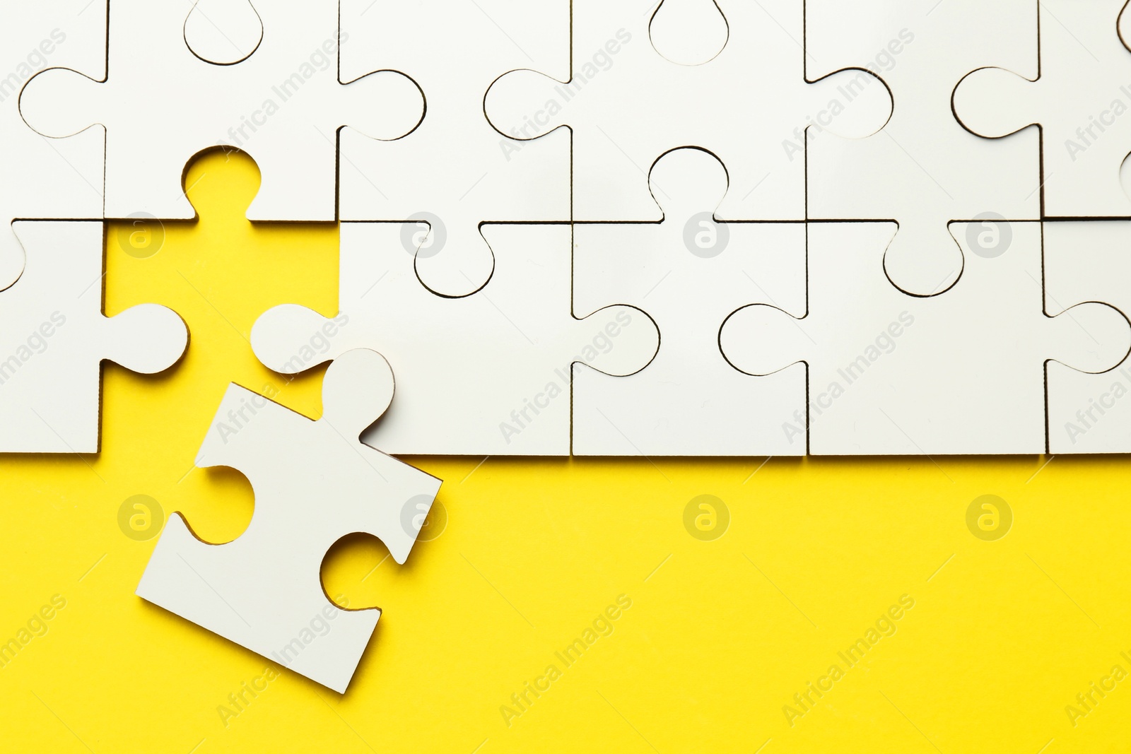 Photo of White puzzle pieces on yellow background, top view