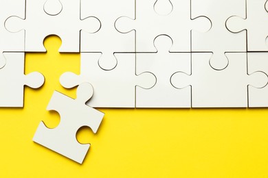 Photo of White puzzle pieces on yellow background, top view