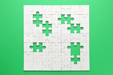 Photo of White puzzle with missing pieces on green background, top view