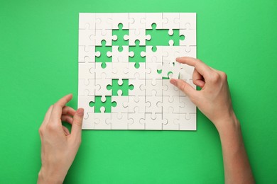 Woman solving white puzzle on green background, closeup