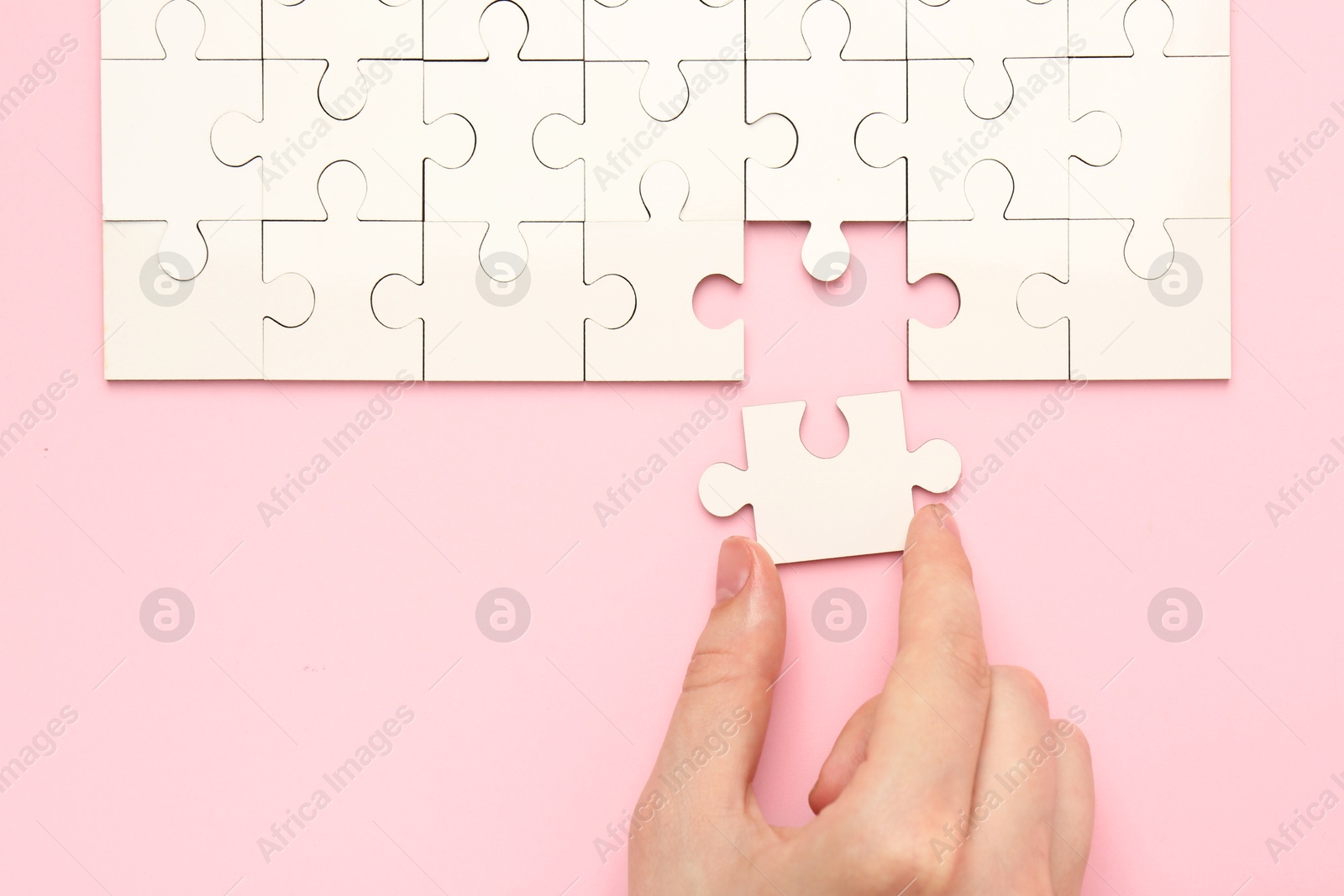 Photo of Woman solving white puzzle on pink background, closeup