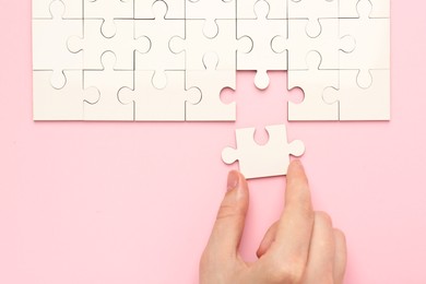 Woman solving white puzzle on pink background, closeup