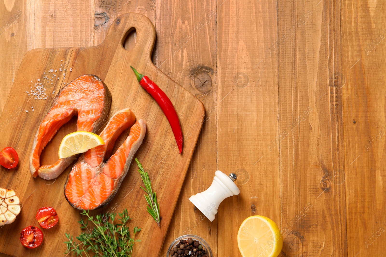 Photo of Tasty grilled salmon steaks, tomatoes, lemon and spices on wooden table, flat lay. Space for text