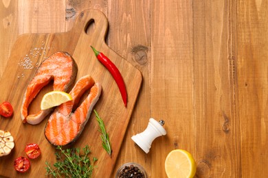 Photo of Tasty grilled salmon steaks, tomatoes, lemon and spices on wooden table, flat lay. Space for text