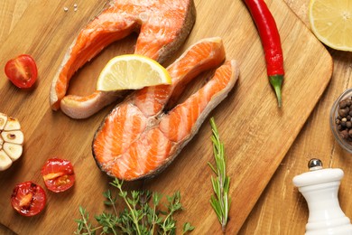 Photo of Tasty grilled salmon steaks, tomatoes, lemon and spices on wooden table, flat lay