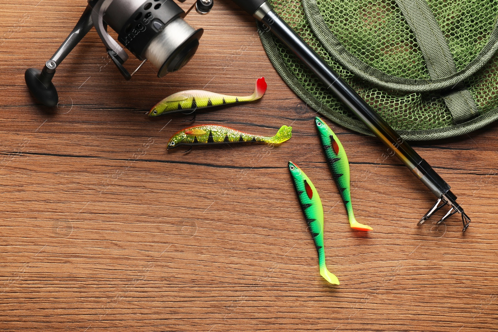 Photo of Fishing rod with spinning reel, baits and net on wooden table, top view. Space for text