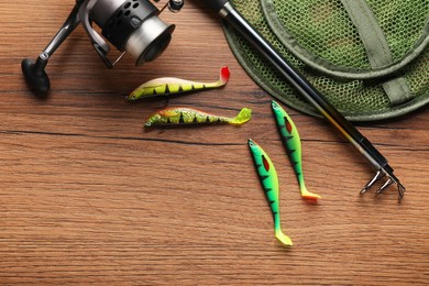 Photo of Fishing rod with spinning reel, baits and net on wooden table, top view. Space for text