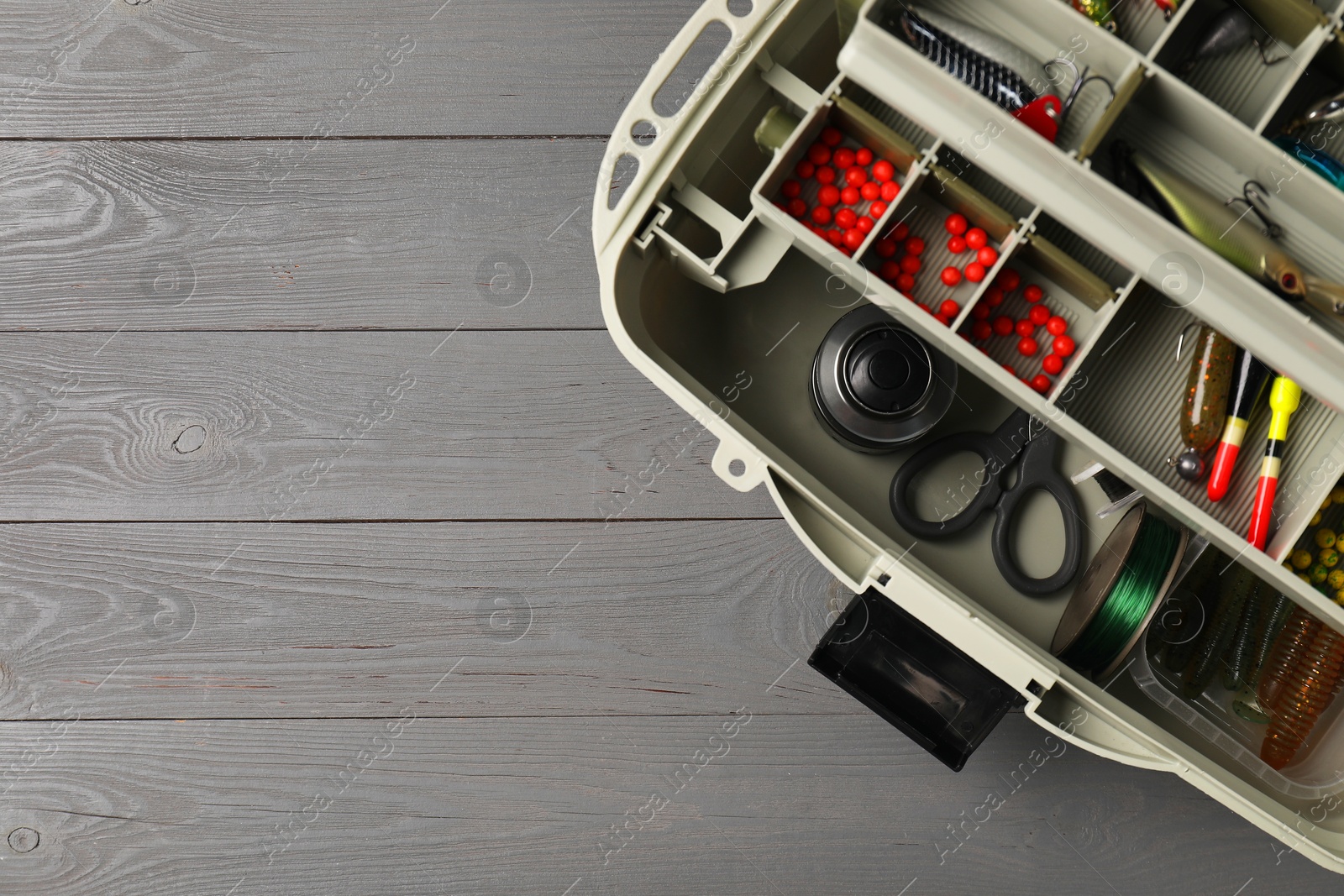 Photo of Different fishing tackles in box on grey wooden table, top view. Space for text