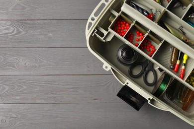 Photo of Different fishing tackles in box on grey wooden table, top view. Space for text