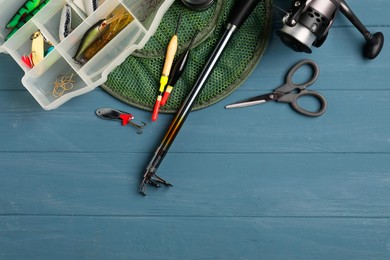 Fishing rod with spinning reel, baits, floats, scissors and net on blue wooden table, top view. Space for text