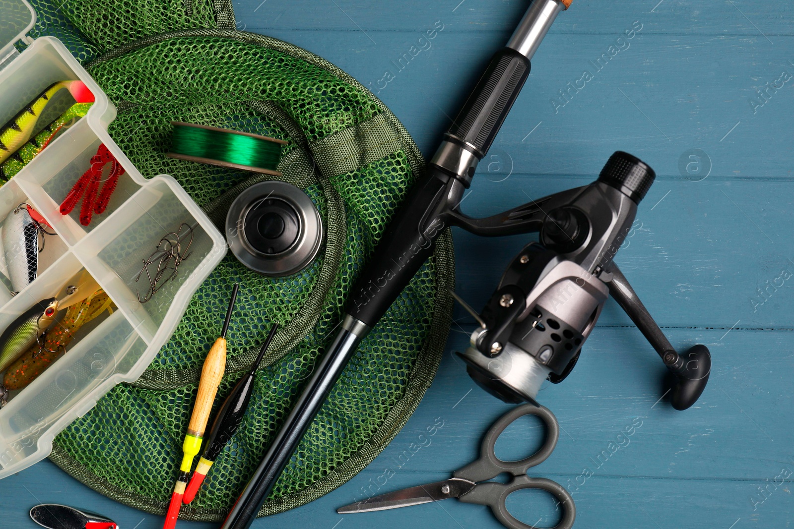 Photo of Fishing rod with spinning reel, baits, floats, scissors, net and line on blue wooden table, top view