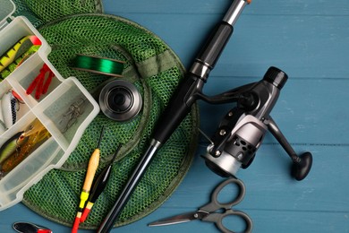 Photo of Fishing rod with spinning reel, baits, floats, scissors, net and line on blue wooden table, top view