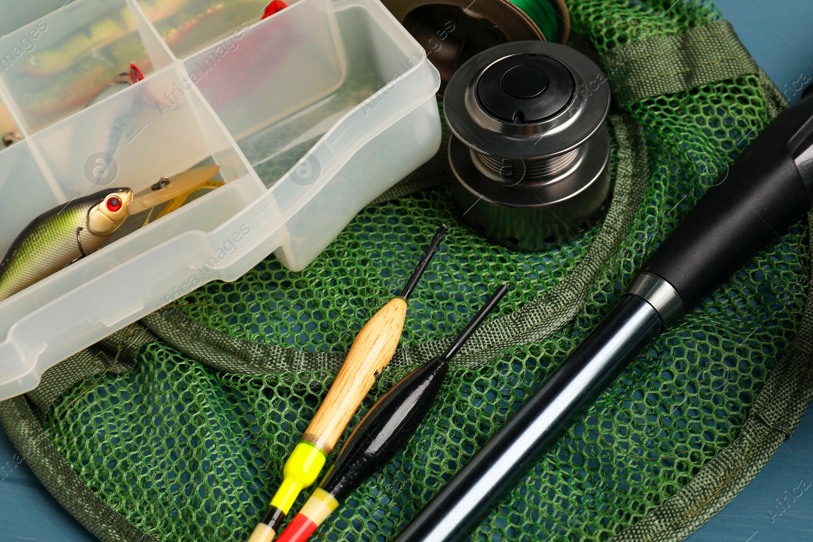 Photo of Fishing rod, spinning reel, floats, net and baits on blue table