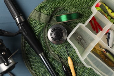 Photo of Fishing rod with spinning reel, baits, floats, net and line on blue wooden table, top view