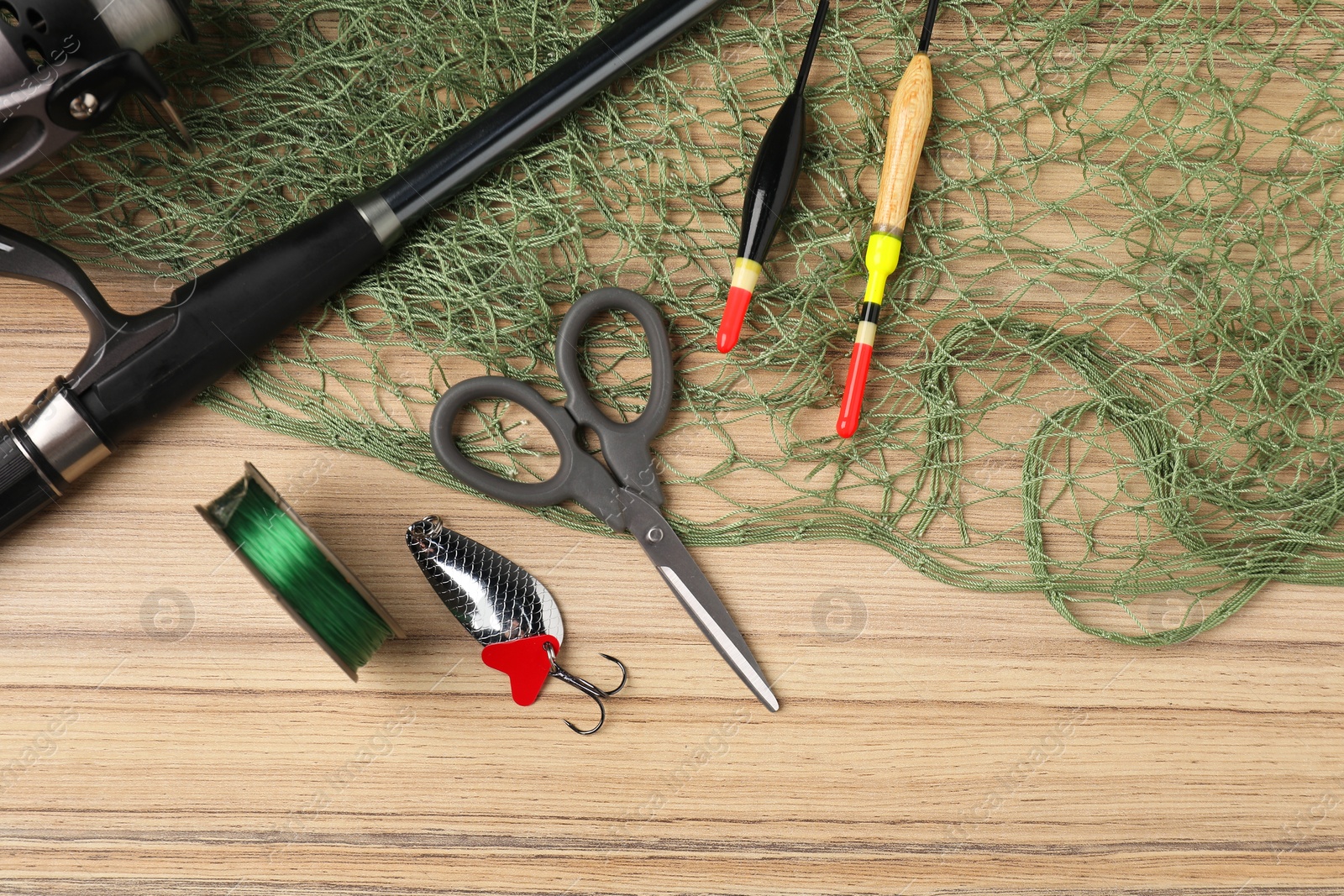 Photo of Fishing rod with spinning reel, bait, floats, line, scissors and net on wooden table, flat lay