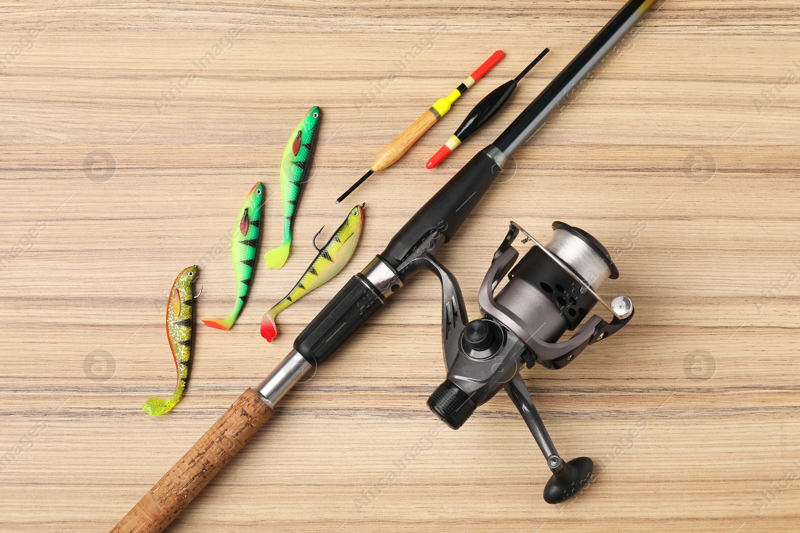 Photo of Fishing rod with spinning reel, baits and floats on wooden table, flat lay