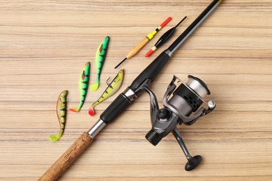 Photo of Fishing rod with spinning reel, baits and floats on wooden table, flat lay