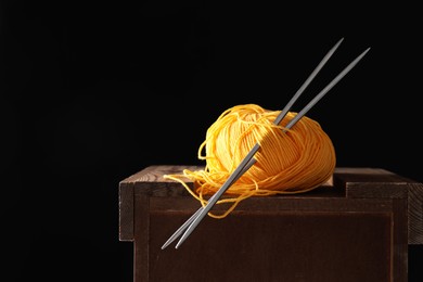 Photo of Skein of orange yarn and knitting needles on wooden stand, space for text