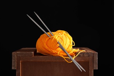 Photo of Skein of orange yarn and knitting needles on wooden stand