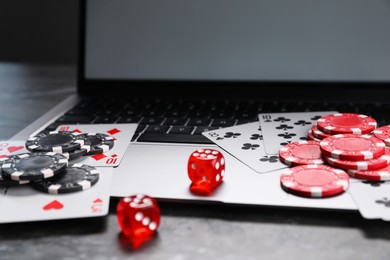 Photo of Poker chips, laptop, playing cards and dices on grey table. Online game