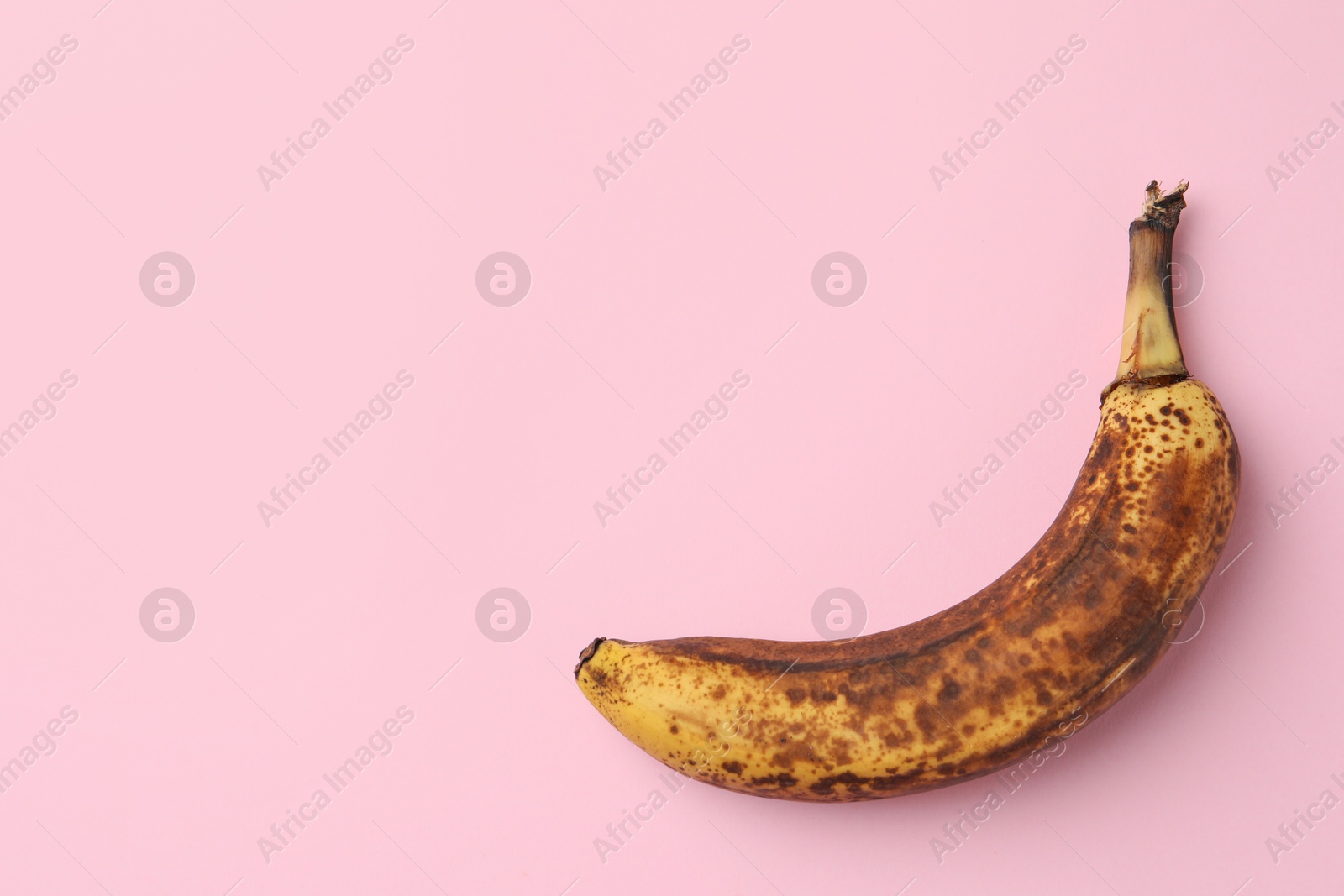 Photo of Overripe banana with dark spots on pink background, top view. Space for text