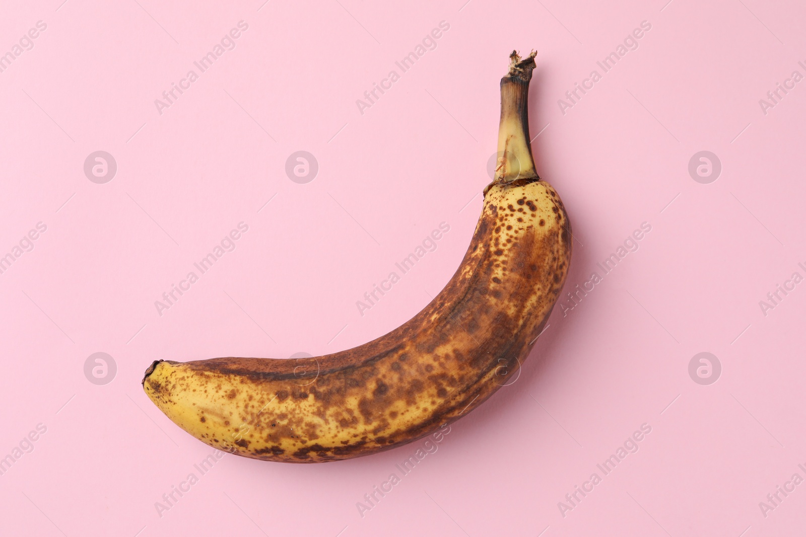 Photo of Overripe banana with dark spots on pink background, top view