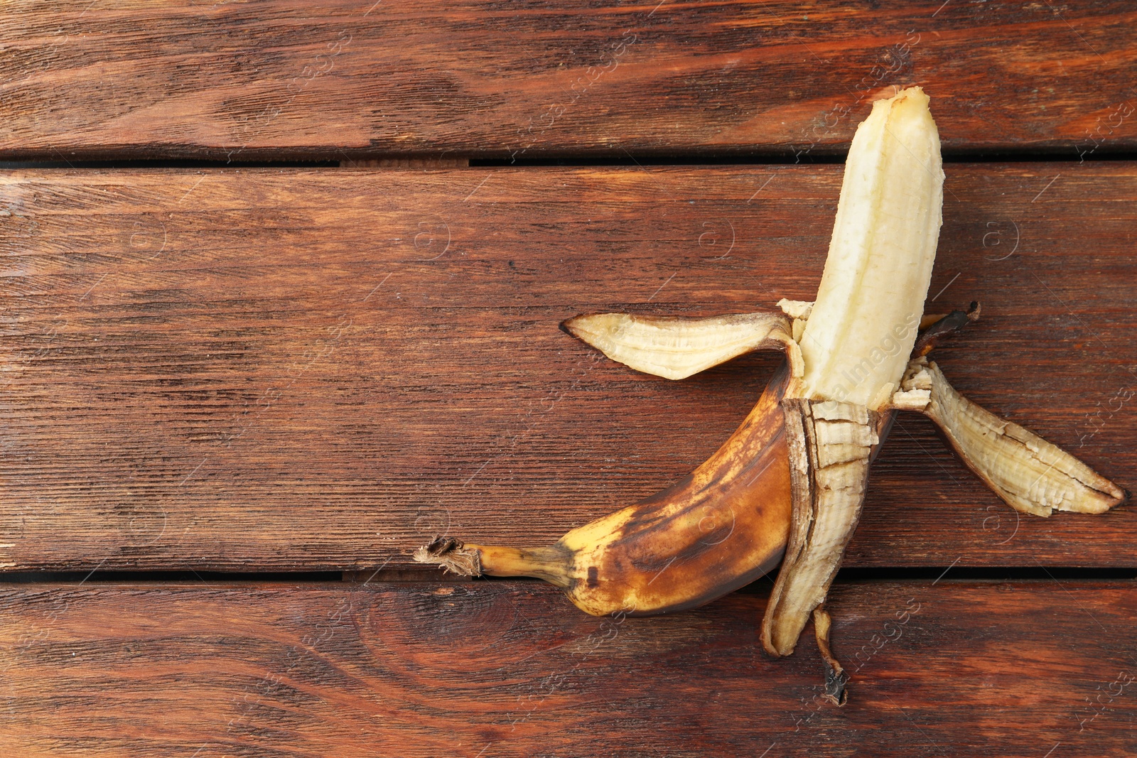 Photo of Overripe banana with dark spots on wooden table, top view. Space for text