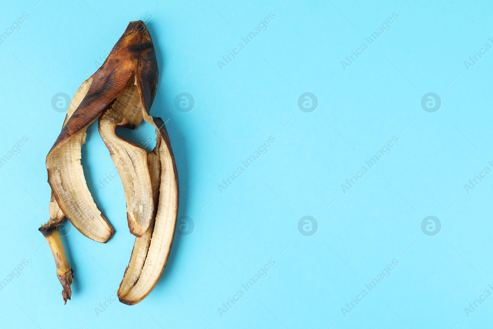 Photo of Banana peel with dark spots on light blue background, top view. Space for text