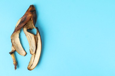 Banana peel with dark spots on light blue background, top view. Space for text