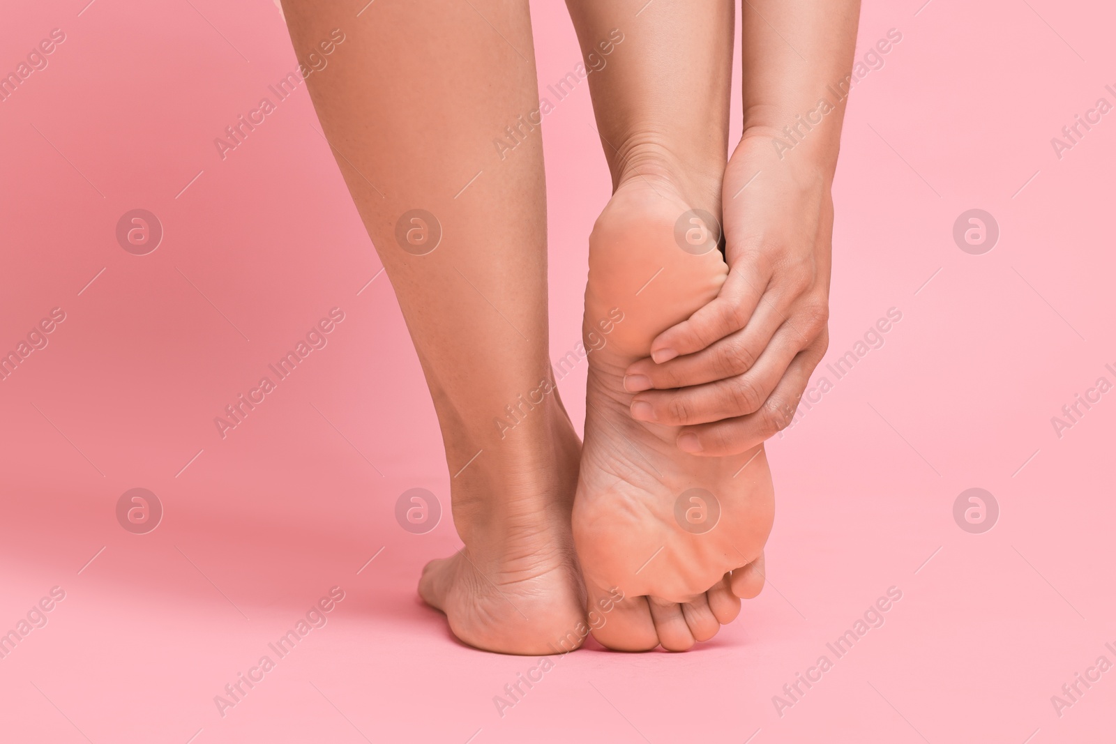 Photo of Woman touching her smooth feet on pink background, closeup