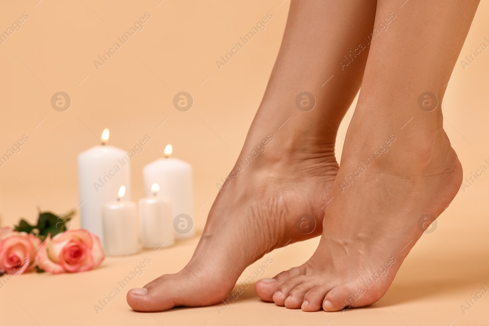 Photo of Woman with smooth feet, burning candles and roses on beige background, closeup