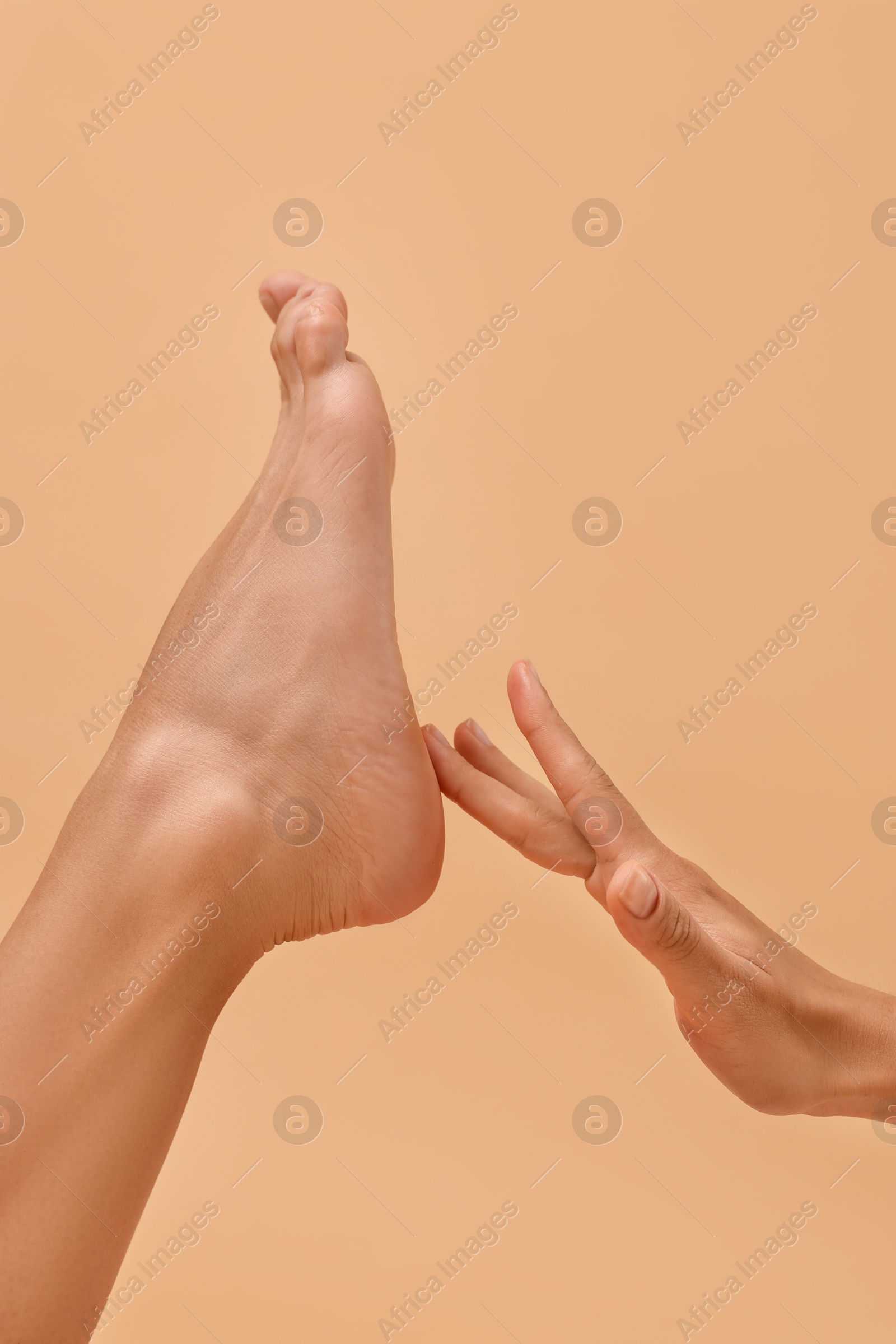 Photo of Woman touching her smooth feet on beige background, closeup