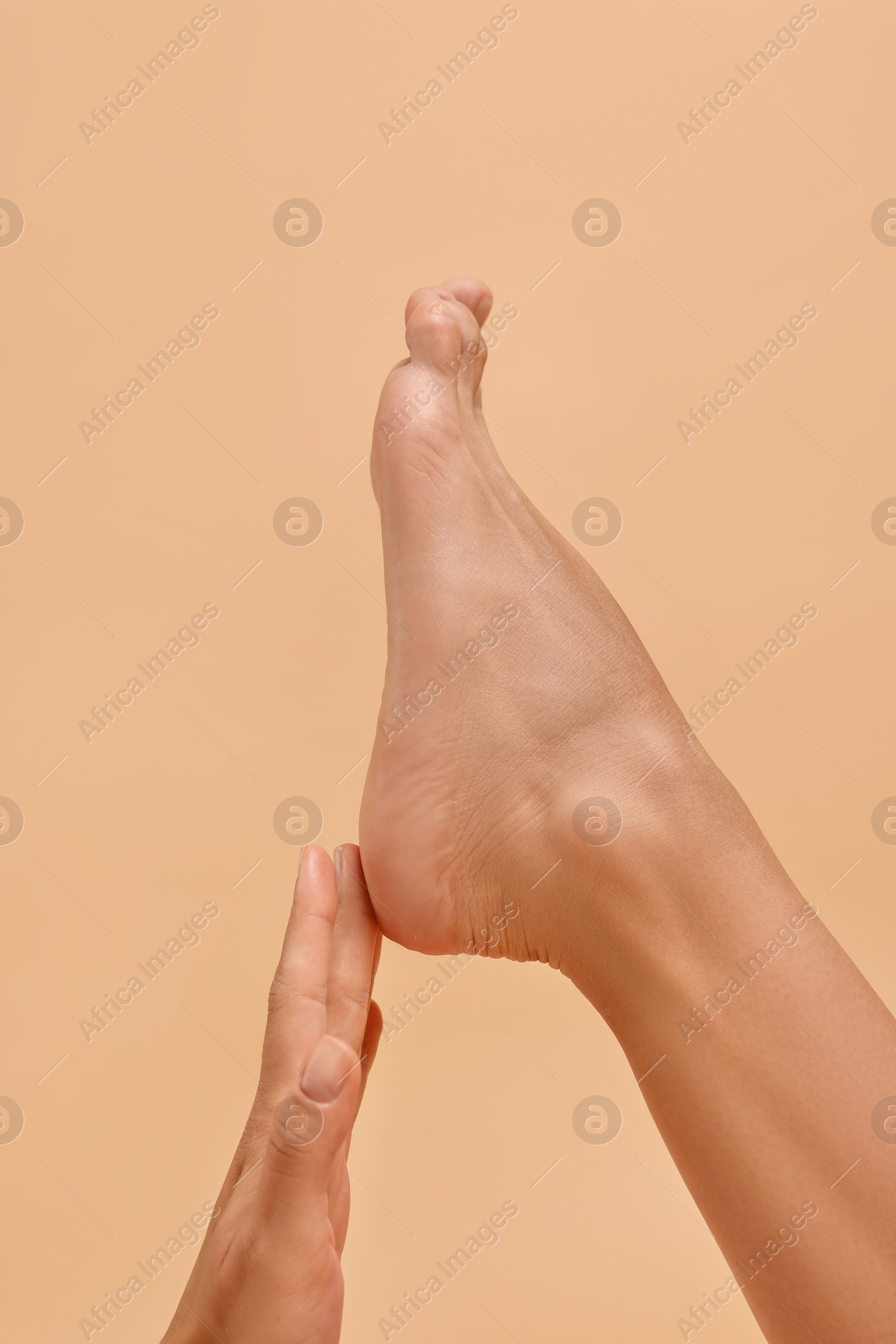 Photo of Woman touching her smooth feet on beige background, closeup