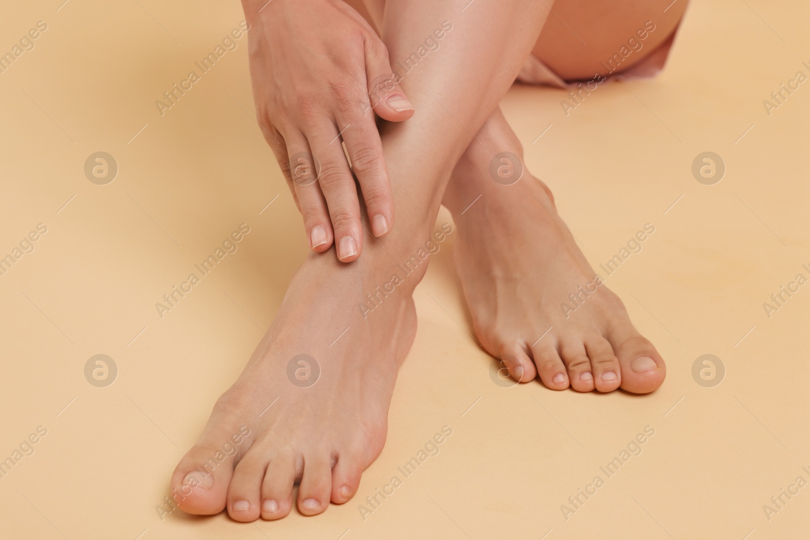 Photo of Woman touching her smooth feet on beige background, closeup