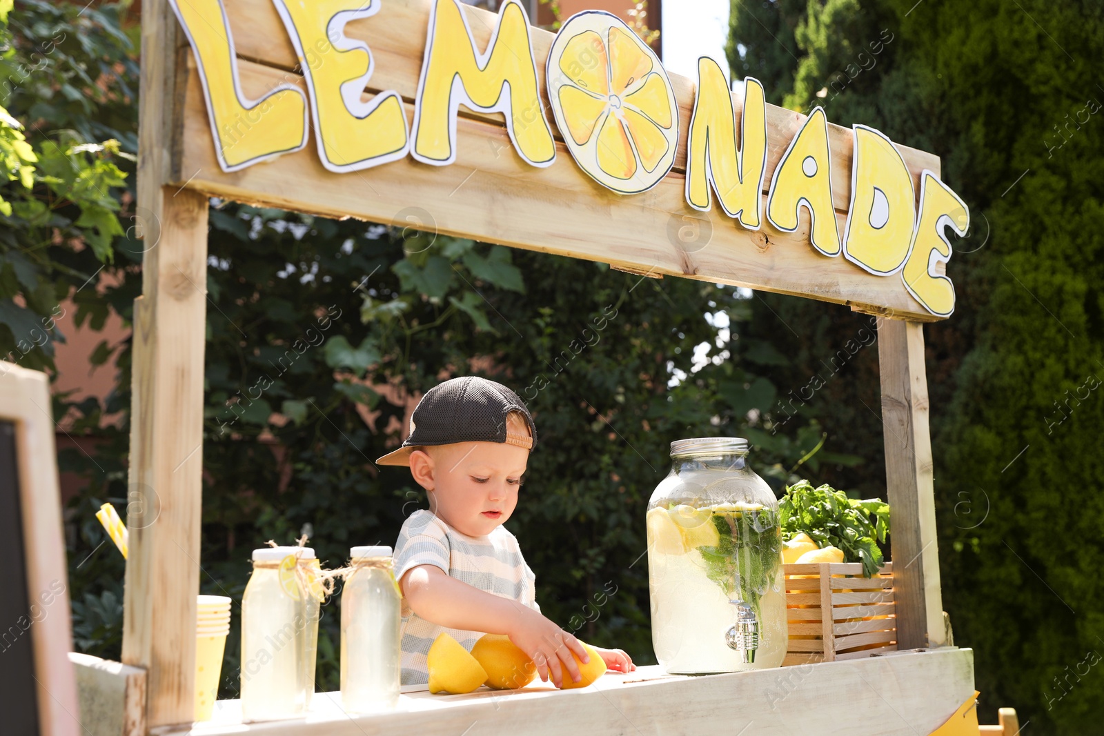 Photo of Cute little boy with lemon at lemonade stand in park