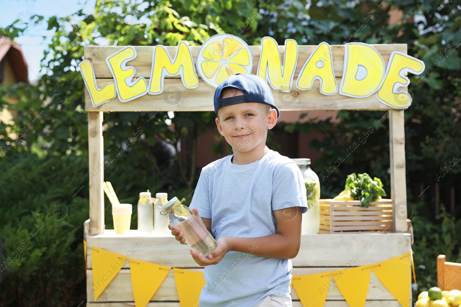 Photo of Cute little boy with refreshing drink near lemonade stand in park