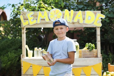 Photo of Cute little boy with refreshing drink near lemonade stand in park