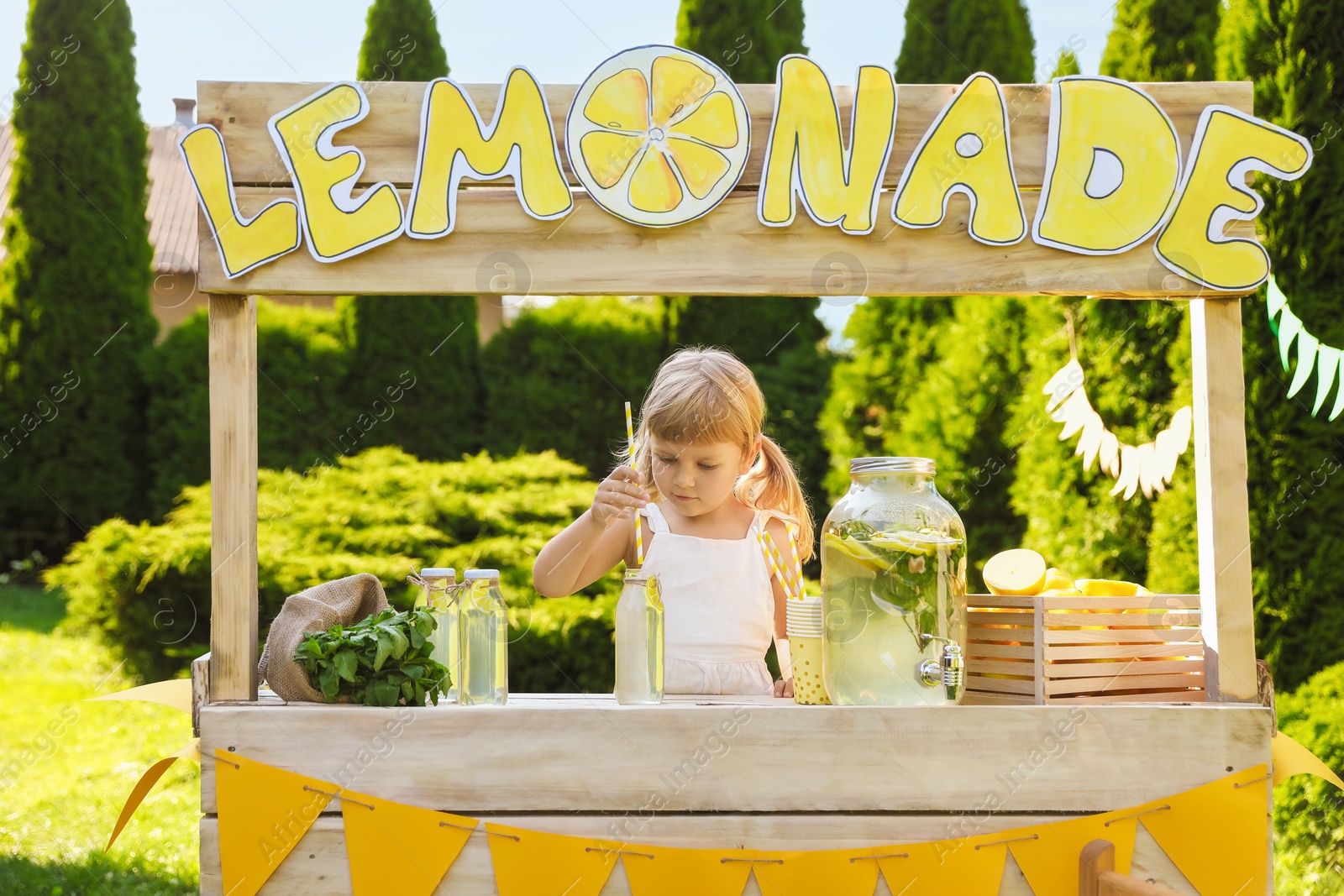 Photo of Cute little girl with refreshing drink at lemonade stand in park