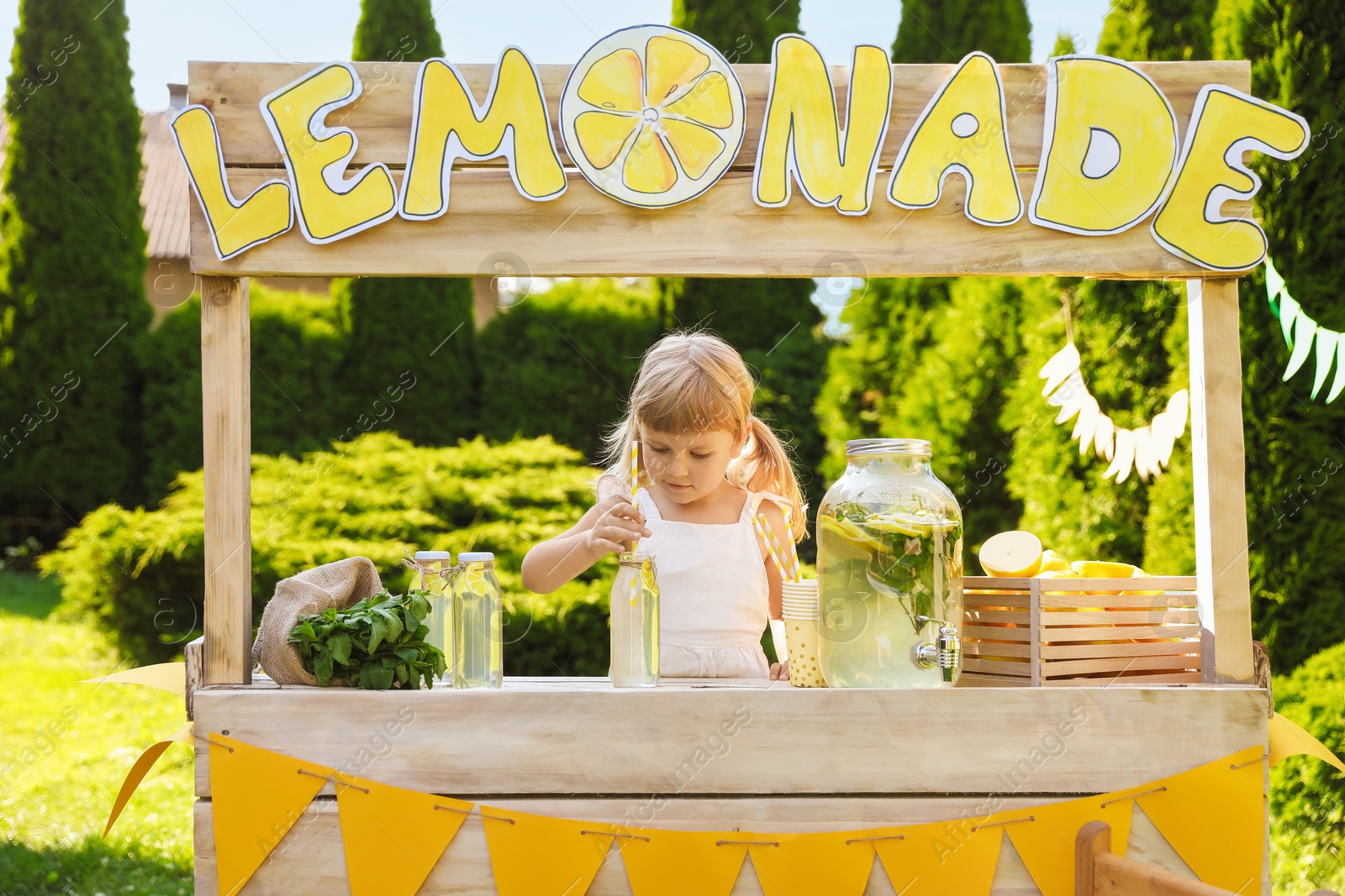 Photo of Cute little girl with refreshing drink at lemonade stand in park